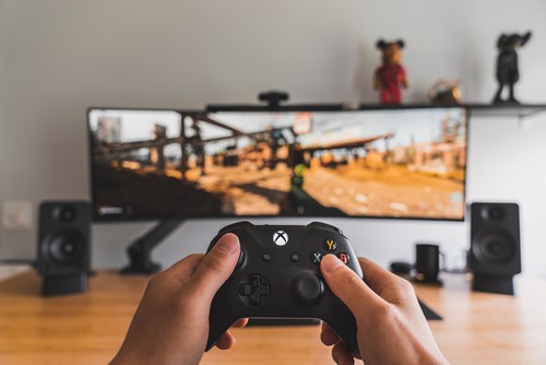 A player using an Xbox controller to play a game on an ultra-wide monitor.