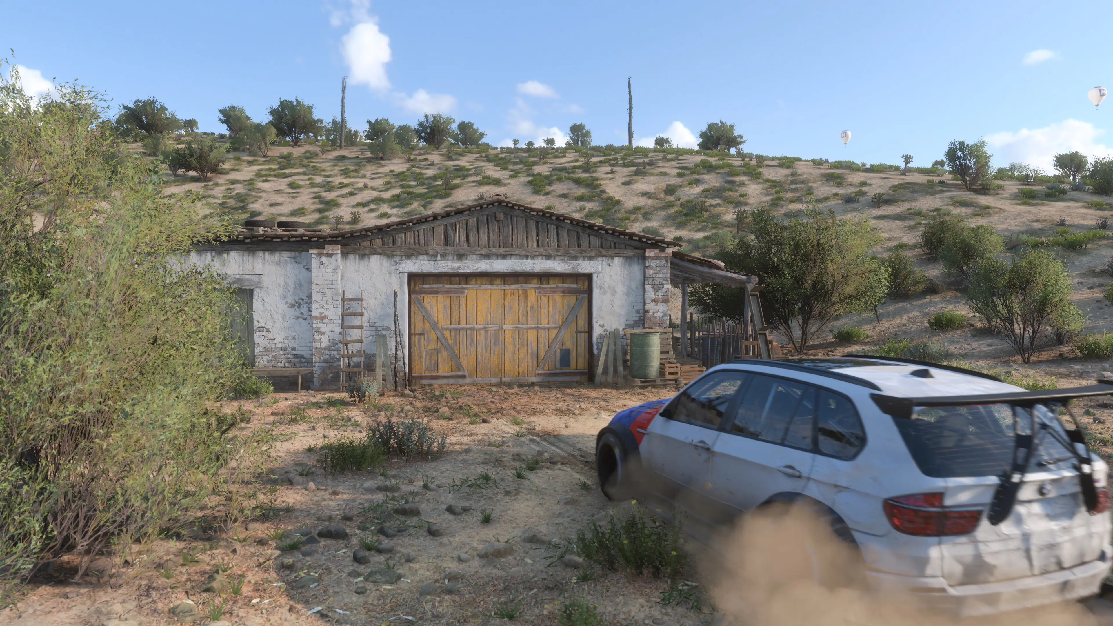 A white car faces a barn in a desert setting.